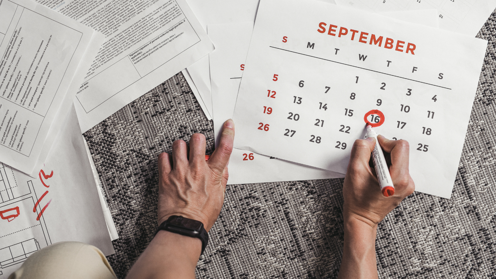 Hand circling a date on a September calendar next to construction drawings